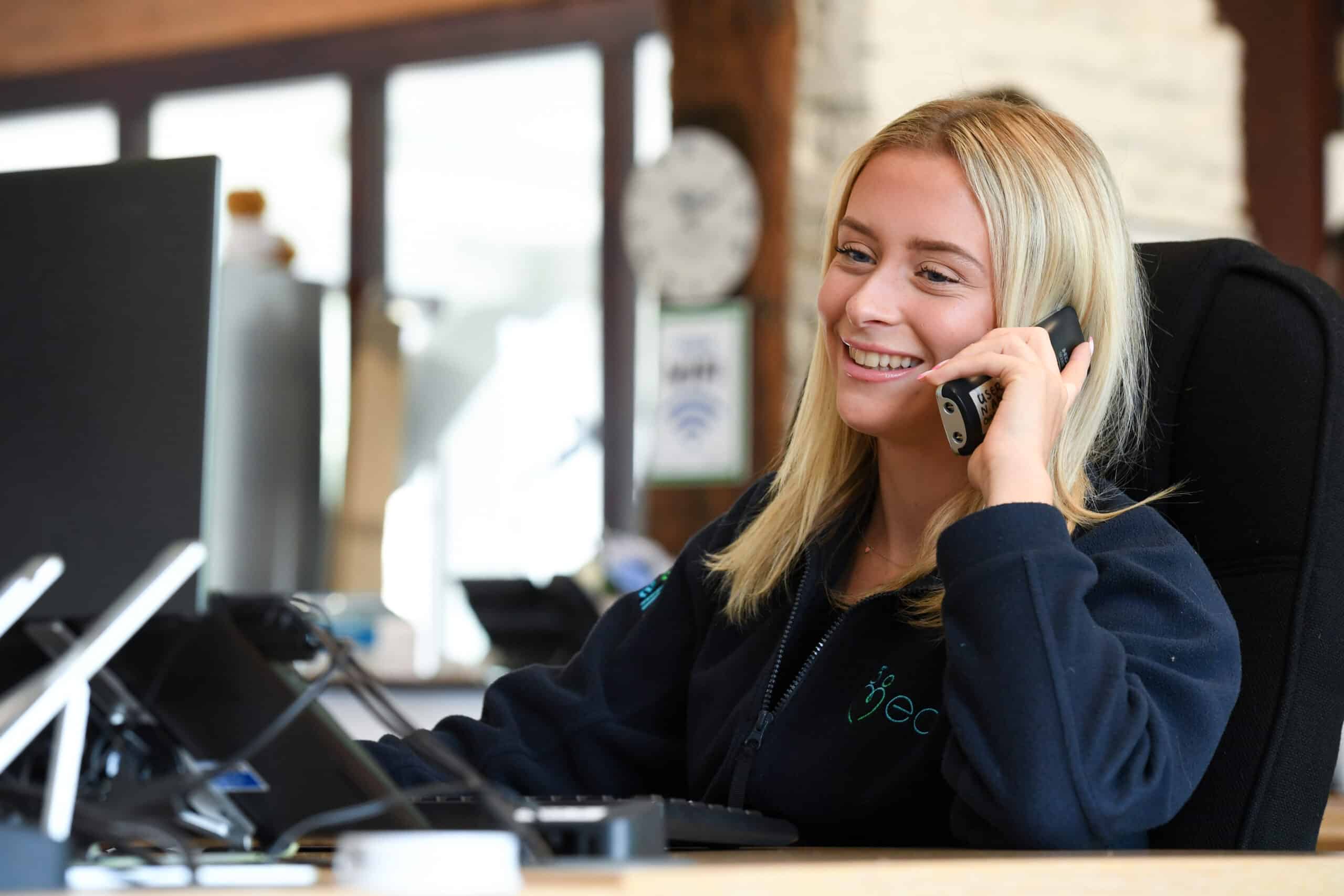 Smiling woman talking on the phone at desk.